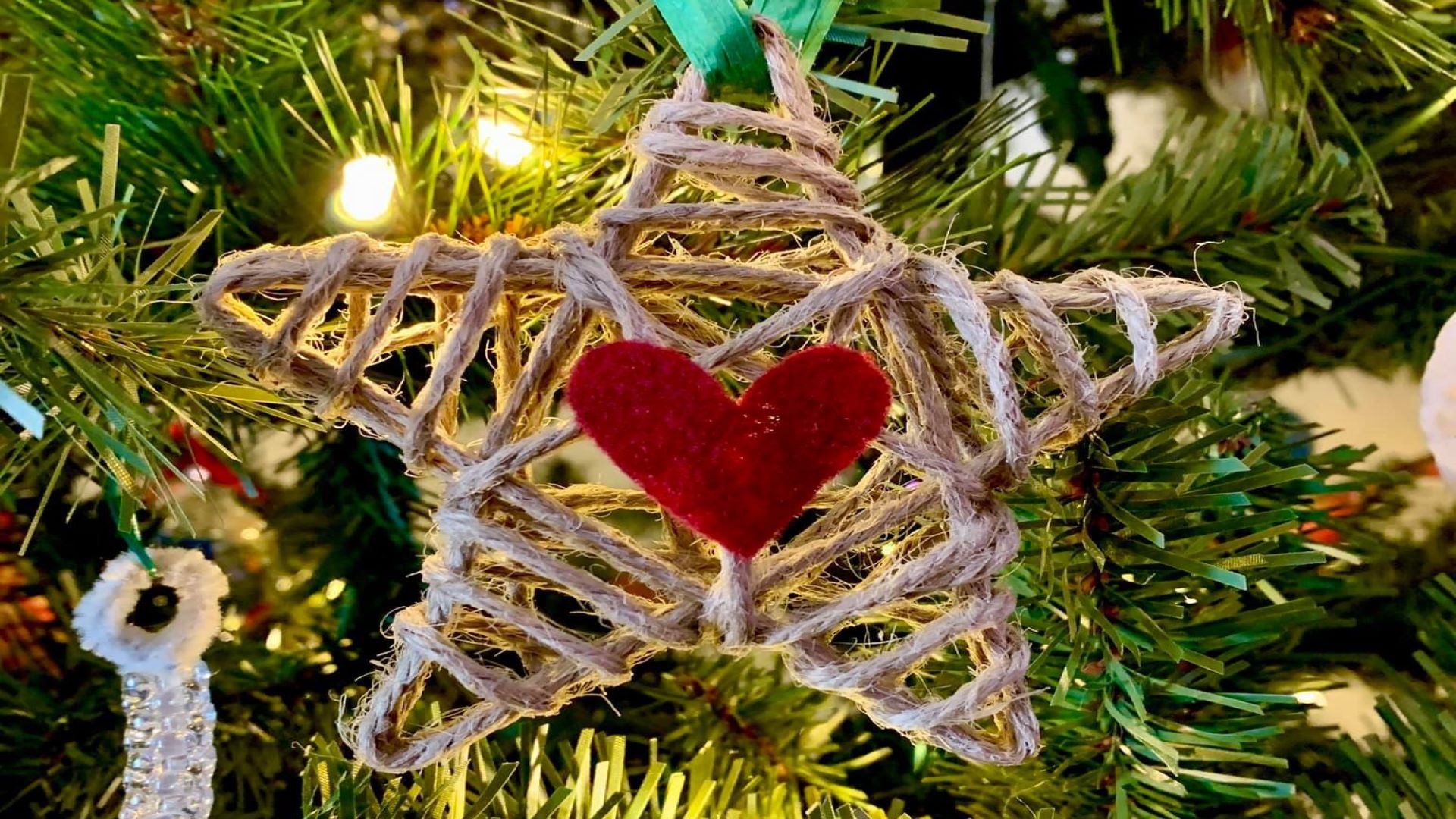 Star shaped Christmas ornament made of twine with a red heart in the center hanging on a Christmas tree.